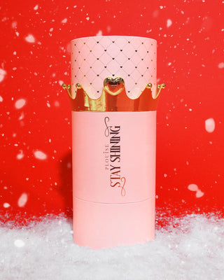 Giant pink cylindrical P.Louise Stay Shining Lip Oil packaging with gold accents on a red background with snow effects
