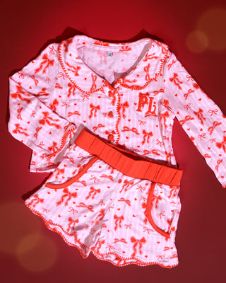 Set of pink and white striped kids christmas pyjamas with red bow designs on them against a red background
