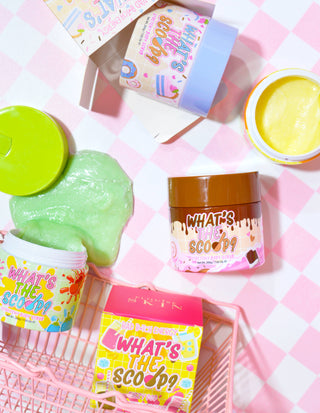 An array of colourful stretchy body scrub containers with the product name 'What's the Scoop?' displayed prominently. The containers are arranged on a surface with a pink checkered background, and there are playful, colourful graphics and text associated with the product.